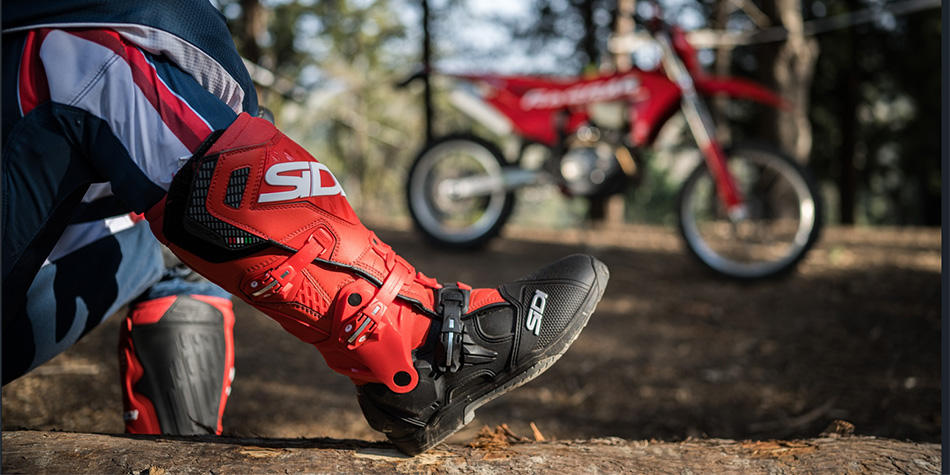 Enduro motorkář v terénních botách a chráničích před jízdou mimo asfalt