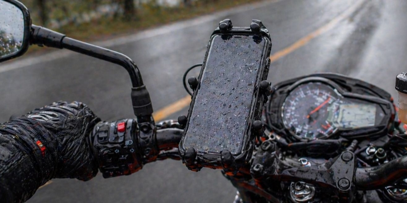 Ochrana mobilu na motorke_ Detail na odolný držiak a mokrý smartfón počas jazdy v daždi