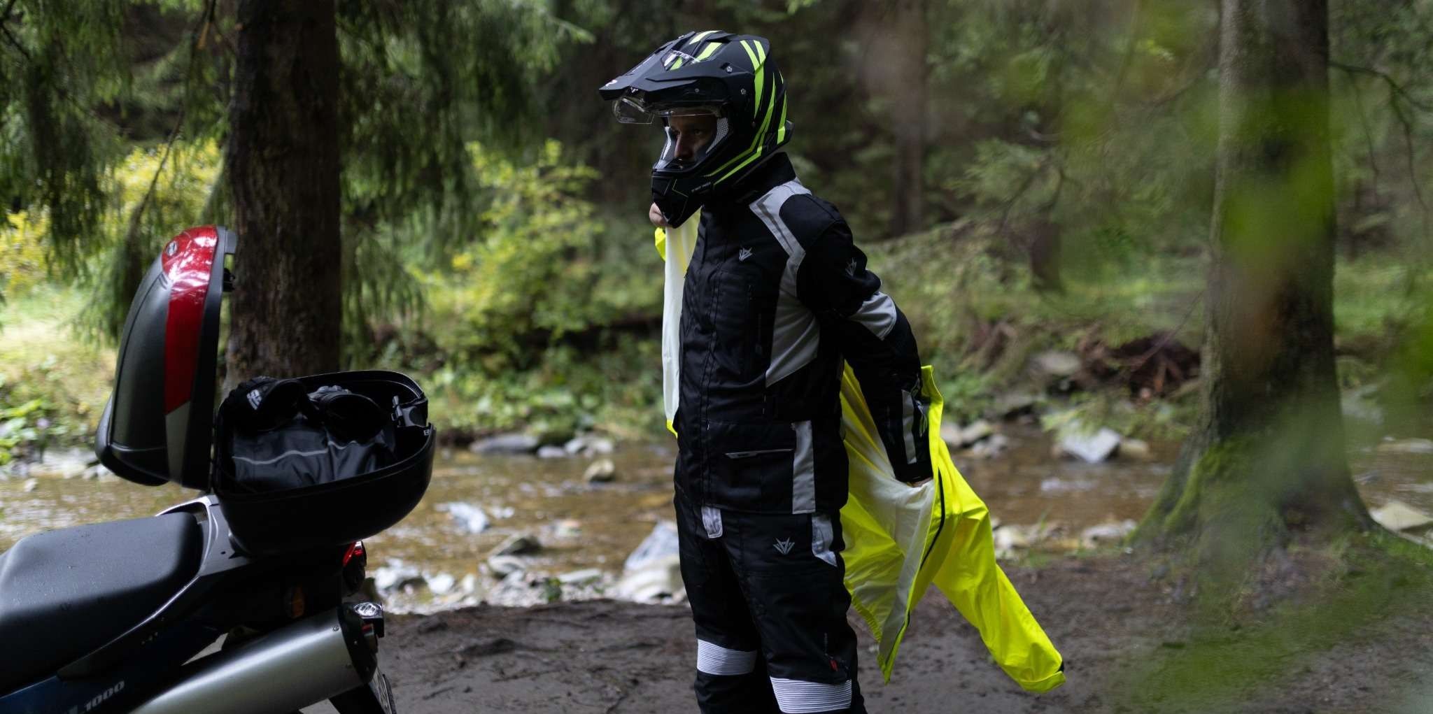 Motorkár v lese si cez moto oblečenie oblieka reflexne žltý nepremok na motorku
