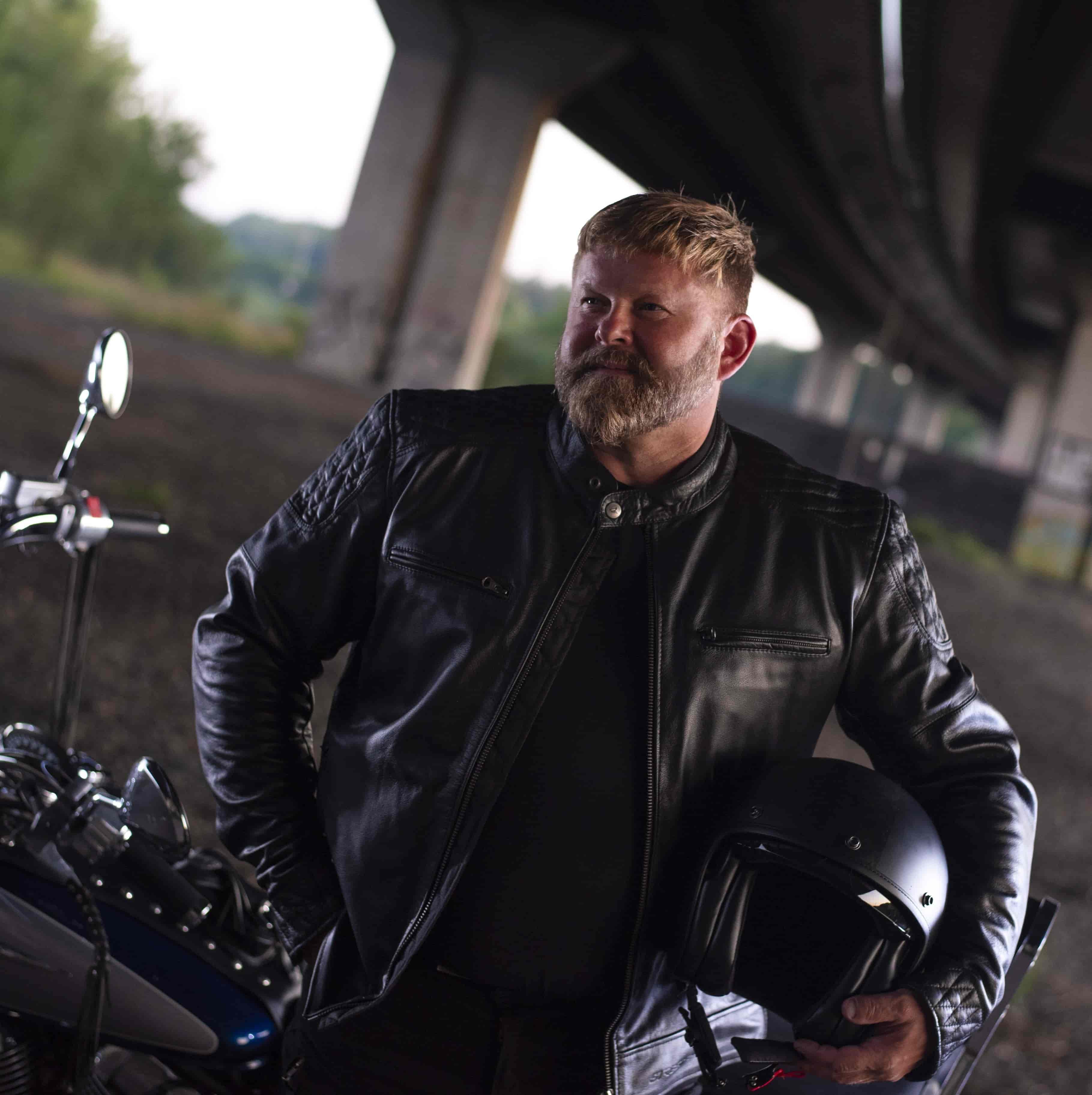 Motorkár v čiernej koženej moto bunde s prilbou pri motocykli